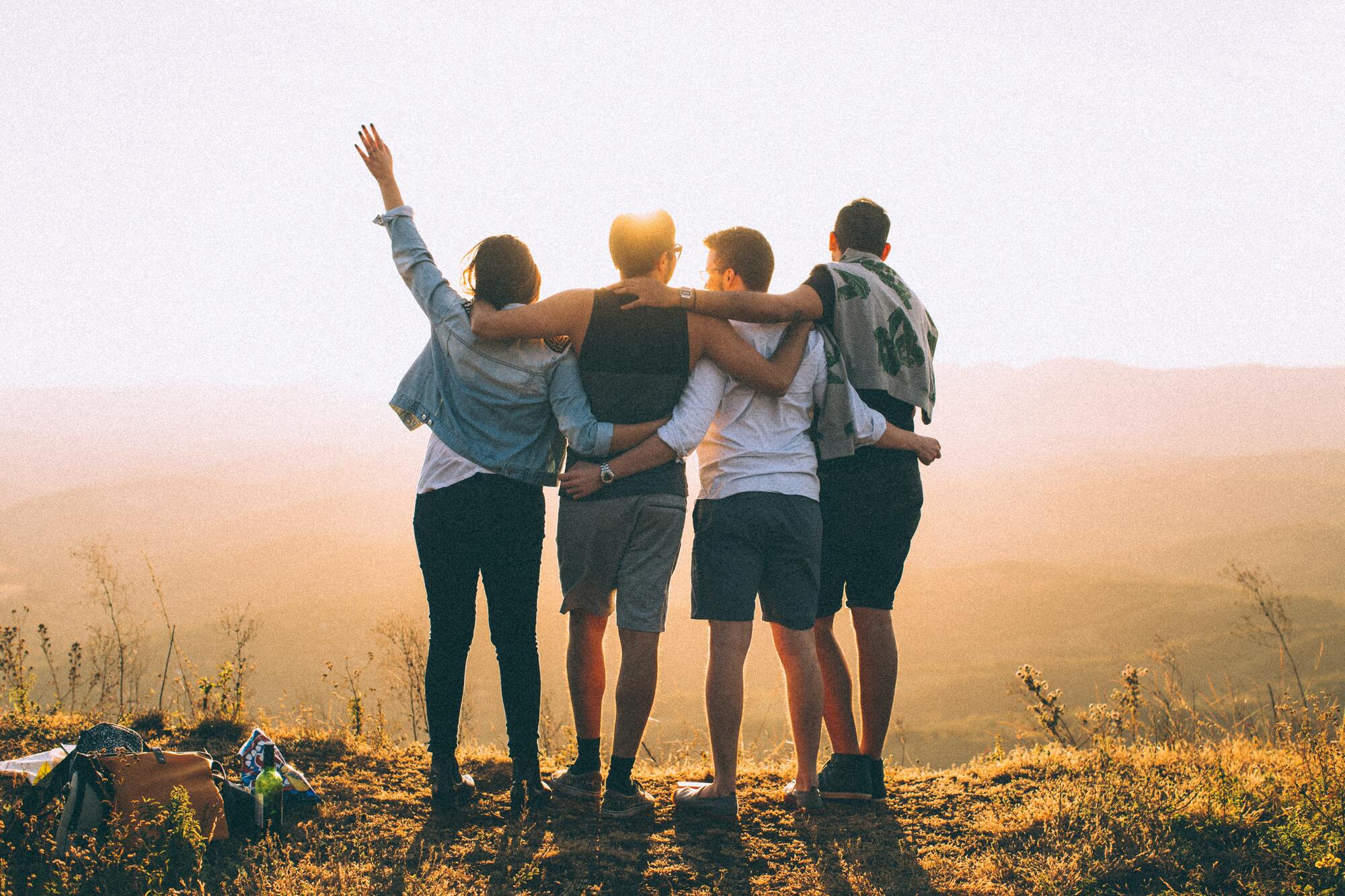 quatre personnes debout se tenant par les épaules devant le soleil