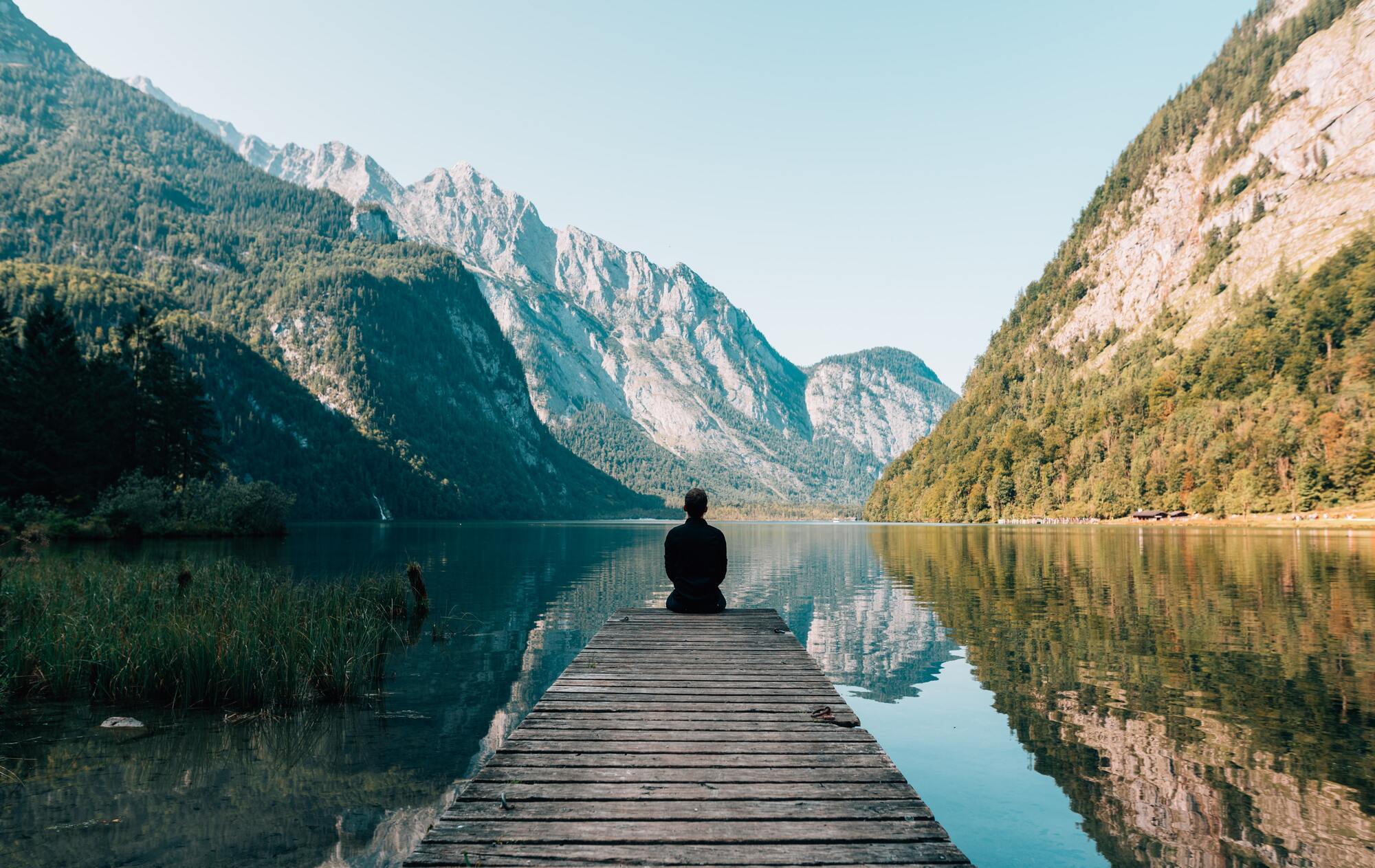une personne assise au bout d'un ponton dans un paysage de lac et de montagne